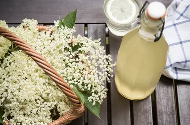 Kwiaty oraz sok z czarnego bzu. Szklanka z sokiem oraz ściereczka na stole.