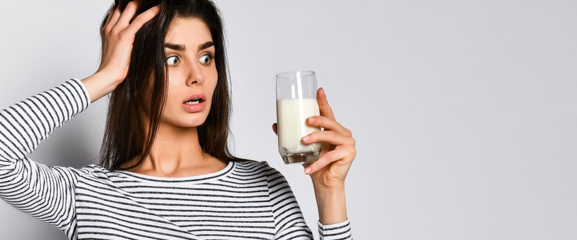 Kobieta trzymająca szklankę mleka w dłoni i zastanawiająca się nad wypiciem mleka