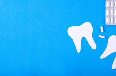 Na niebieskim tle narysowane dwa białe zęby oraz tabletki.