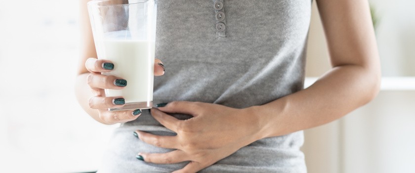 Kobieta trzymająca szklankę mleka i trzymająca się za brzuch.