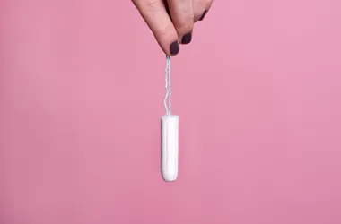 Kobieta trzymająca za sznurek tampon na różowym tle.
