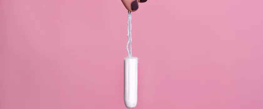 Kobieta trzymająca za sznurek tampon na różowym tle.