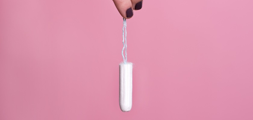 Kobieta trzymająca za sznurek tampon na różowym tle.