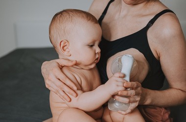 Młoda mama trzyma niemowlaka na kolanach i ściąga sobie pokarm z piersi