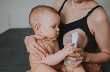 Młoda mama trzyma niemowlaka na kolanach i ściąga sobie pokarm z piersi