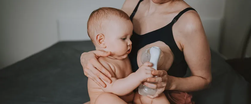 Młoda mama trzyma niemowlaka na kolanach i ściąga sobie pokarm z piersi