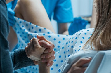 Kobieta podczas porodu w szpitalu. Mężczyzna trzyma kobietę za dłoń podczas porodu.