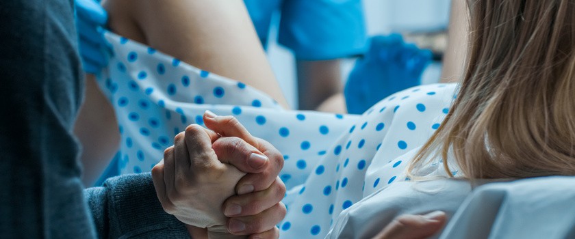 Kobieta podczas porodu w szpitalu. Mężczyzna trzyma kobietę za dłoń podczas porodu.