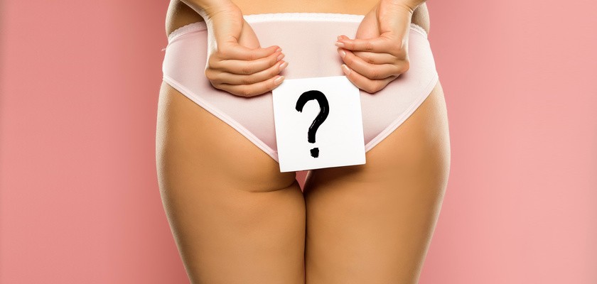 Kobieta stojąca tyłem w bieliźnie, trzymająca kartkę ze znakiem zapytania