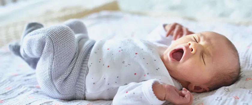 Niemowlę przeciągające się w białym body oraz szarych spodenkach w łóżeczku