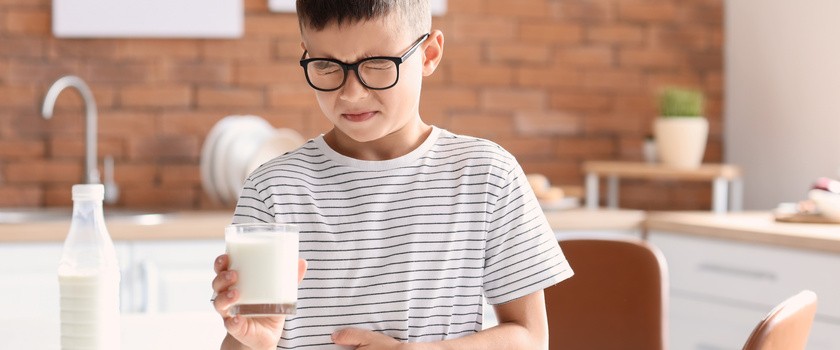 Mały chłopiec w koszulce w paski ze szklanką mleka w dłoni i trzymający się za brzuch