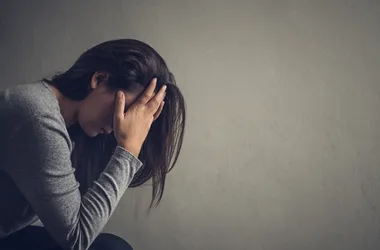 Przygnębiona, samotna kobieta siedzi na krześle w ciemnym pokoju w domu.