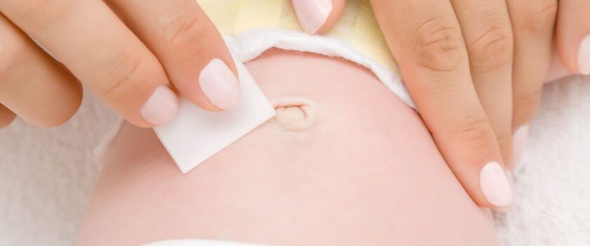 Kobiece dłonie czyszczące okolice pępka noworodka. Wydzielina z pępka.