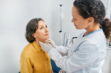 Lekarz dotyka szyi dojrzałej kobiety w celu diagnostyki chorób tarczycy i niedoczynności tarczycy.