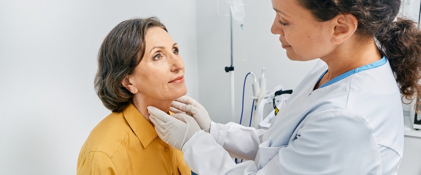 Lekarz dotyka szyi dojrzałej kobiety w celu diagnostyki chorób tarczycy i niedoczynności tarczycy.