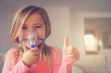 Dziewczynka podczas przeprowadzania inhalacji, trzymająca kciuk w górę.