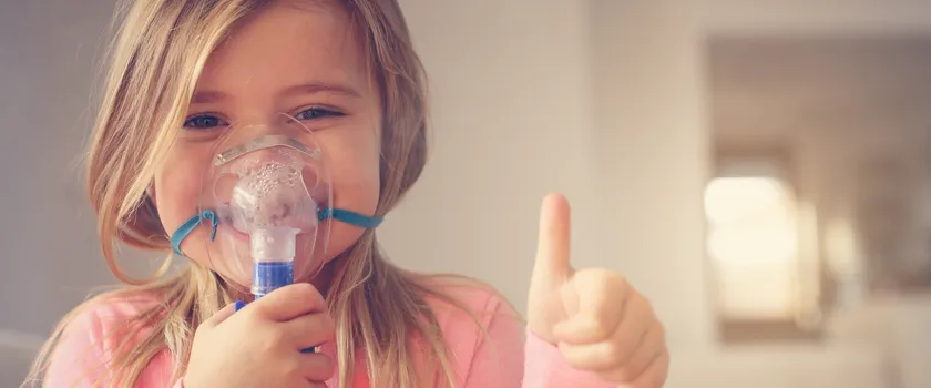 Dziewczynka podczas przeprowadzania inhalacji, trzymająca kciuk w górę.