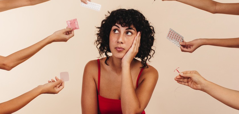 Kobieta zastanawiająca się nad wyborem odpowiedniej metody antykoncepcji. Z prawej i lewej stronie dłonie z poszczególnymi środkami antykoncepcji.