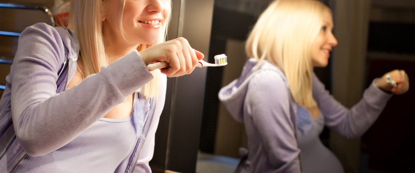Kobieta w ciąży trzymająca szczoteczkę do zębów z nałożoną pastą.