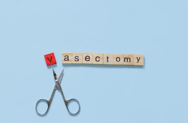 Ułożony napis "Vasectomy" z literek do Scrable na błękitnym tle. Poniżej nożyczki.