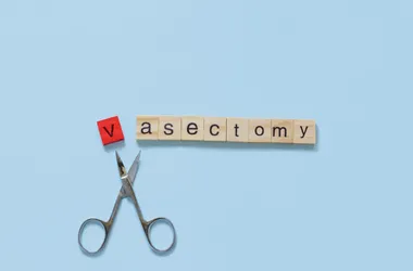 Ułożony napis "Vasectomy" z literek do Scrable na błękitnym tle. Poniżej nożyczki.