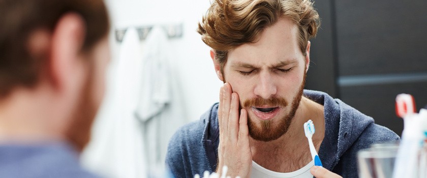 mężczyzna z bólem dziąseł podczas mycia zębów