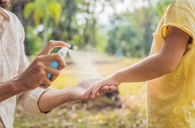 Tata i syn używają sprayu na komary. Rozpylanie środka odstraszającego owady na skórze na zewnątrz