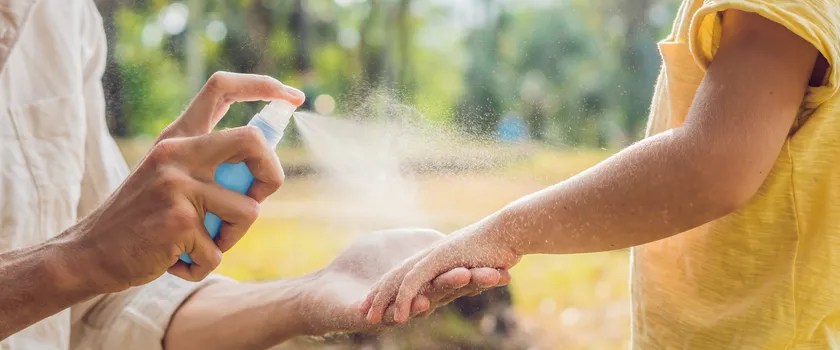 Tata i syn używają sprayu na komary. Rozpylanie środka odstraszającego owady na skórze na zewnątrz