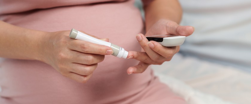 Kobieta w ciąży trzymająca glukometr i samodzielnie sprawdzająca poziom cukru we krwi w domu.