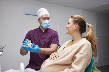Kobieta w ciąży siedzi na fotelu w gabinecie i rozmawia ze stomatologiem.
