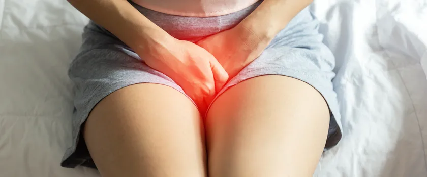 Kobieta siedząca na łóżku w sypialni i czująca ból w okolicach stref intymnych