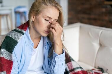 Zmęczona i zdenerwowana kobieta dotykająca grzbietu nosa, odczuwająca zmęczenie oczu lub ból głowy, próbując złagodzić ból.