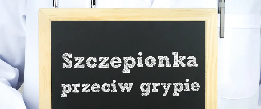 Lekarz w kitlu oraz z stetoskopem trzymający tablice z napisem "Szczepionka przeciw grypie".