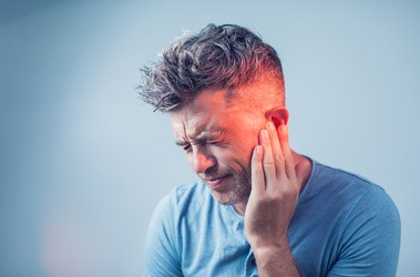 Mężczyzna trzymający się za ucho z powodu bólu