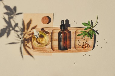 Olej CBD, nalewka z pipetą oraz tabletka na drewnianej desce na beżowym tle z liśćmi konopi.