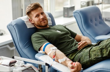 Uśmiechnięty młody mężczyzna na fotelu podczas oddawania krwi w centrum dawców.