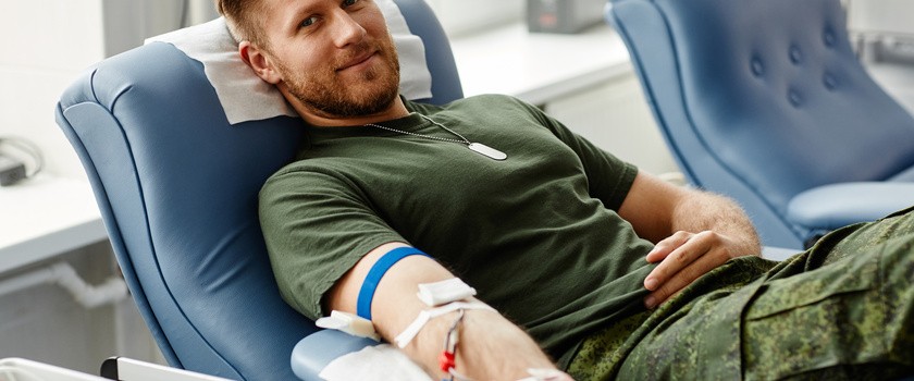 Uśmiechnięty młody mężczyzna na fotelu podczas oddawania krwi w centrum dawców.