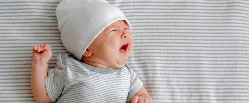 Płaczący noworodek w czapce leżący na szarej pieluszce w paski.