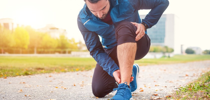 Mężczyzna cierpiący na ból kostki kuca z bólu