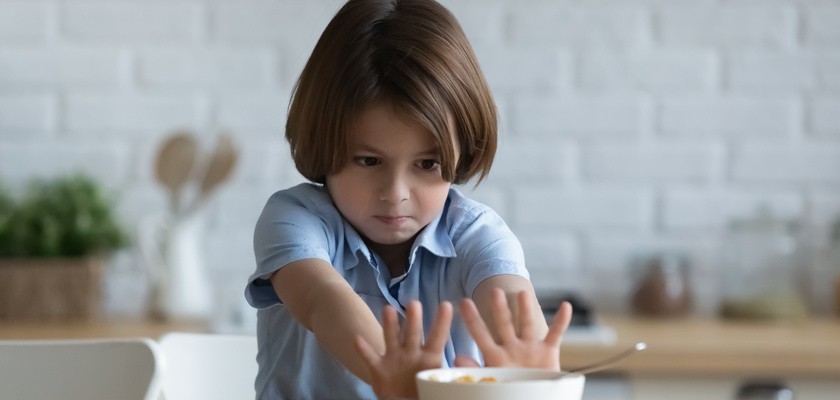Chłopiec w dłuższych włosach odsuwa od siebie miseczkę z jedzeniem