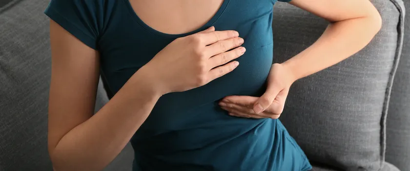 Kobieta w niebieskiej bluzce trzymająca się za biust