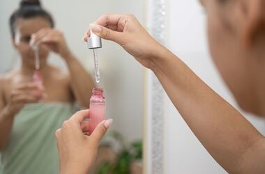 Kobieta przed lustrem nakłada serum na twarz. Peptydy na twarz, peptydy w kosmetykach. 