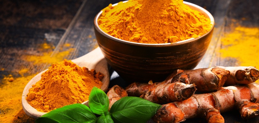 Kompozycja z miską z kurkumą na drewnianym stole obok natomiast cała kurkuma