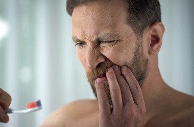 Mężczyzna trzymająca się za twarz po umyciu zębów