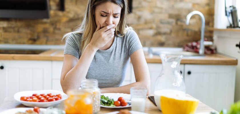 Młoda kobieta czuje mdłości podczas śniadania przy stole jadalnym.