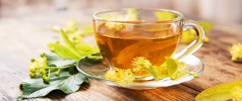 herbata z lipy w przezroczystym kubku na drewnianym stole. obok leżą liście i kwiaty lipy