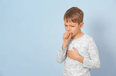 Chłopiec kaszlący na niebieskim tle.