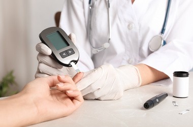 lekarz sprawdzający poziom cukru we krwi pacjenta za pomocą glukometru w gabinecie