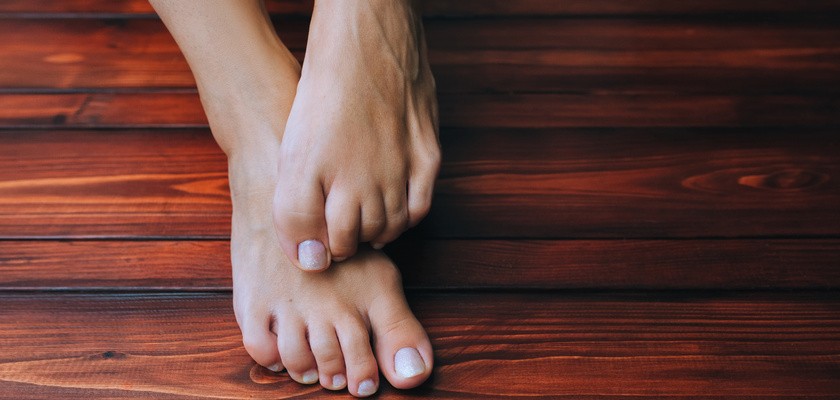 Kobiece stopy na tle brązowej drewnianej podłogi z bliska. Swędzenie i drapanie z powodu grzybicy.