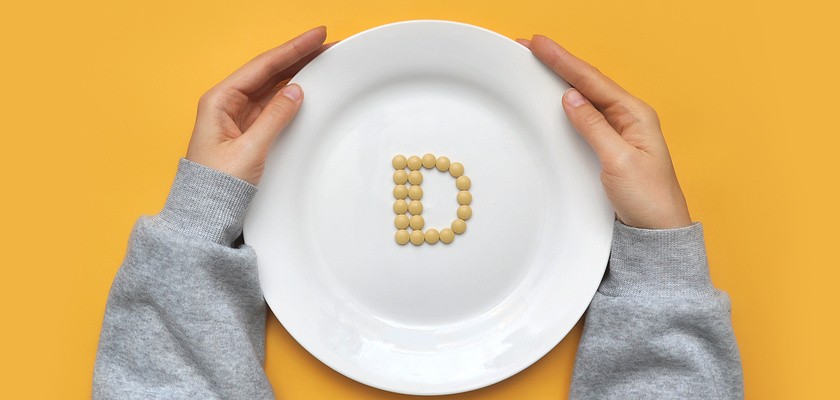 Osoba trzyma w ręce biały talerz. Litera D ułożona z tabletek witaminy D.